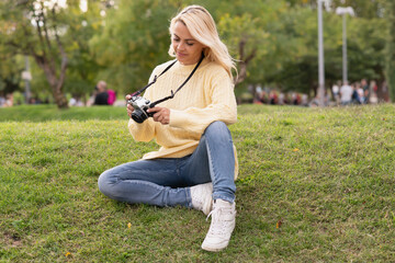 Fototapeta premium Blonde woman sitting on a park while using a camera