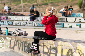 Sportive blonde woman listening to music while sitting in skate park