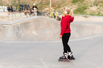Blonde woman with inline skates and headphones standing in a skate park