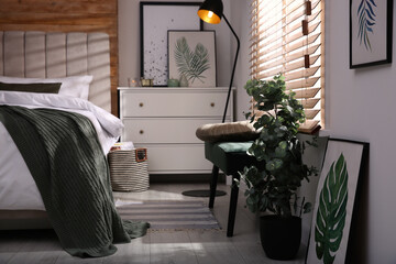Stylish bedroom interior with green eucalyptus tree, floral paintings and bench