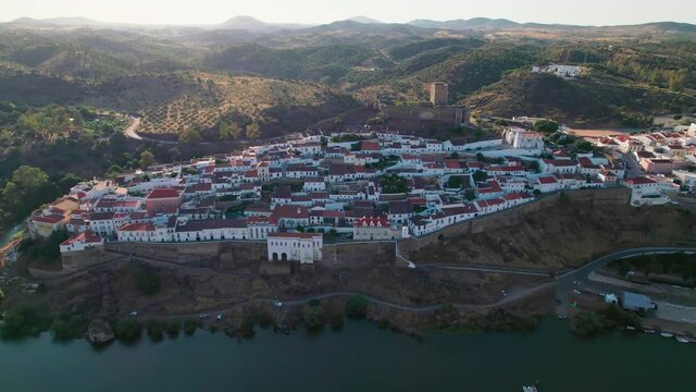 Beautiful Portuguese landscape village with a medieval castle and bridge in 4K. Drone footage from above of Castle of Mertola surrounded by many traditional colored houses by a river in Beja, Portugal