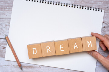 「DREAM」と書かれた積み木、ノート、ペン、人の手 - obrazy, fototapety, plakaty