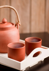 clay cups with hot steam, with tea on white wooden tray, with kettle, brown wooden background.
