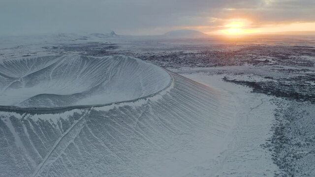 Breathtaking drone footage of snowy tephra cone or tuff ring volcano during beautiful sunrise in background - Cold frozen winter day on Iceland showing Hverfjall Volcano system reserve
