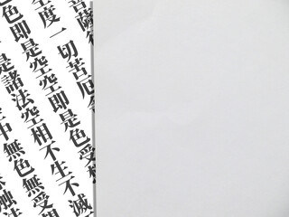 横長の紙に斜めの『般若心経』の一部と灰色の紙のコピースペース。仏教、宗教、東洋のイメージ素材。真上からの撮影。