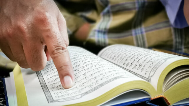 Close up man finger pointing on verse in Holy Al Quran.