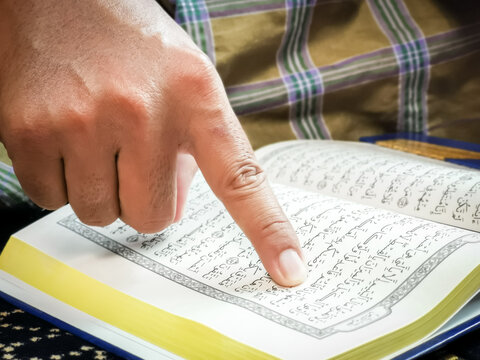 Close up man finger pointing on verse in Holy Al Quran.