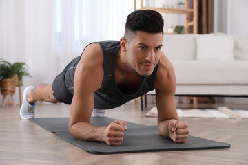 Handsome man doing plank exercise on yoga mat at home
