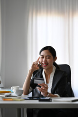 Attractive businesswoman holding credit card and talking on mobile phone with customer service.