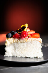 Slice of pavlova, an Australian dessert, with fresh fruit including strawberries, raspberries, blueberries, passionfruit pulp and whipped cream.