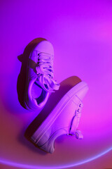 Trendy fashion white sneakers on abstract bright background. Neon lights on casual shoes. Orange and violet gradient light. Minimalism, 90s concept.