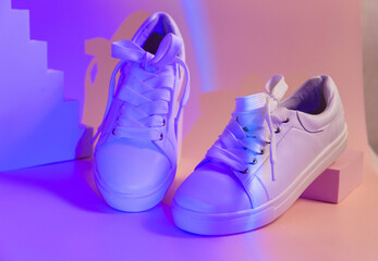 Trendy fashion white sneakers on geometry podium on abstract bright background. Neon lights on casual shoes. Violet and orange gradient light. Minimalism, 90s, 80s concept.