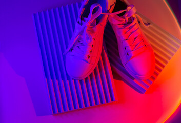 Trendy fashion white sneakers on geometry podium on abstract bright background. Neon lights on...