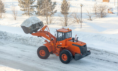 Big orange tractor cleans up snow from the road and loads it into the truck. Cleaning and cleaning...