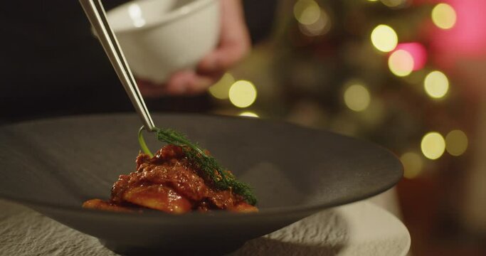 Close up shot of hands of male chef decorating a pasta plate with fennel on top using kitchen tweezers