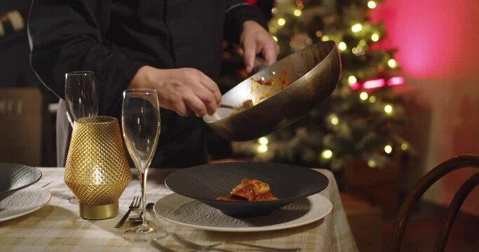Close up shot of unrecognizable chef serving gourmet pasta in a holiday scene with a blurred christmas tree