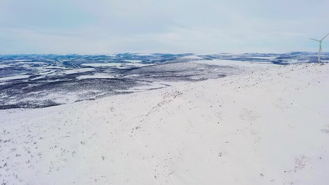 Aerial view of a mountain and arctic wilderness with windmills, winter in Enontekio, Finland - reverse, tilt, drone shot