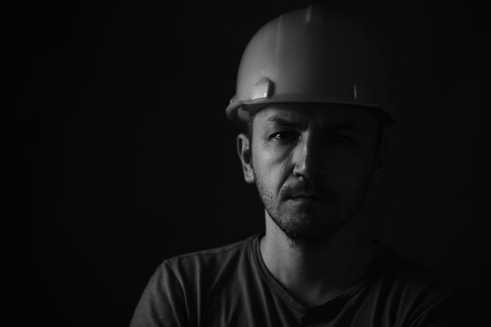 Dirty face of coal miner on a black background. Head of tired mine worker in a hard hat. Black and white photographic portrait.