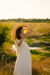 Young beautiful girl in a white dress having a picnic with a glass of champagne or white wine. Romantic picnic. Happy beautiful girl on the nature picnic. Summer time