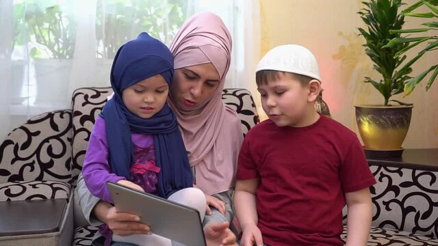 Remote online education of children. Happy traditional Muslim family, mother in hijab and children together at home using a tablet calls to the teacher during Covid-19 lockdown
