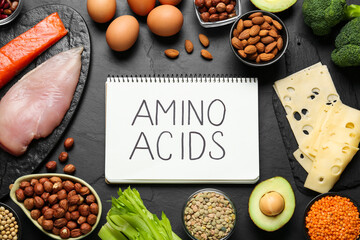 Different fresh products and notebook with words Amino Acids on black table, flat lay