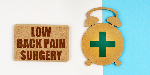 On the white and blue surface are an alarm clock and a sign with the inscription - Low Back Pain Surgery