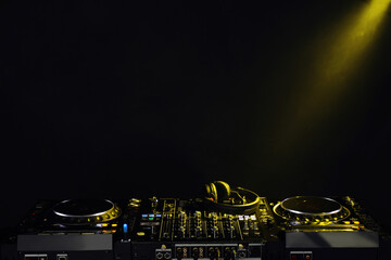 Modern DJ controller and headphones under beam of light on black background