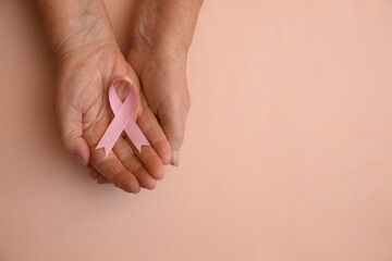Senior woman holding pink ribbon on beige background, top view with space for text. Breast cancer awareness