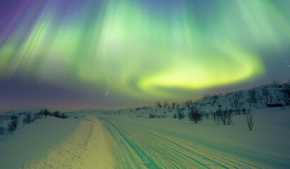 Beautiful winter landscape with snow and ice covered road - Northern lights (Aurora borealis) in the sky over Tromso, Norway