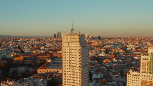 Elevated shot of town development lit by bright sunset light. Torre de Madrid historic high rise building in foreground.