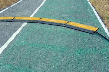 Black and yellow heavy plastic covers for people and vehicle to cross over cables laid on road. Pavement pads to protect electrical wiring on sidewalk in public park. Channel for laying the wires.
