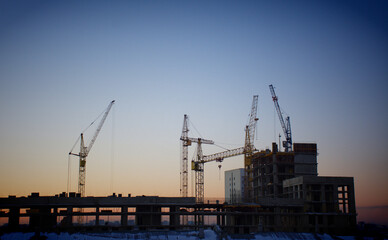 Fototapeta na wymiar Construction cranes are building a house against the background of sunset and dark sky