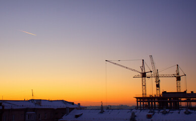 Cranes build a house against the background of sunset and dark sky