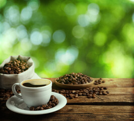 Cup of aromatic hot coffee and beans on wooden table outdoors. Space for text