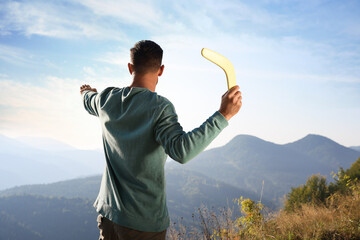 Man throwing boomerang in mountains on sunny day, back view - obrazy, fototapety, plakaty