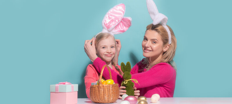 Mother and child daughter celebrating Easter. Cute little girl with funny face in bunny ears laughing, smiling and having fun isolated on blue. Easter banner with copy space.
