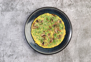 Mushroom Omelet with herbs on a round plate on a dark grey background. Top view, flat lay