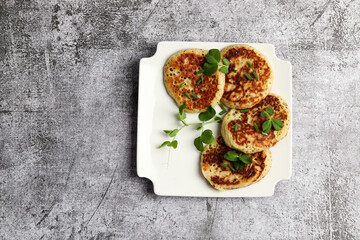 Potato Pancakes with herbs on a white square  plate on a dark background. Top view, flat lay