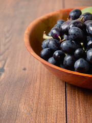 Fresh dark grapes in a wooden bowl and on a wooden table. Agriculture product. Vertical image.