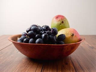 Fresh mango and dark grapes in a small wooden bowl and table. Still life. Light and rich saturated color.