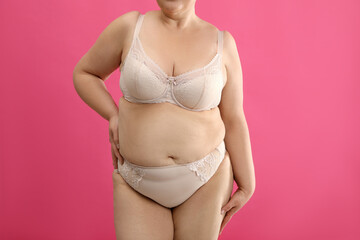 Overweight woman in beige underwear on pink background, closeup. Plus-size model