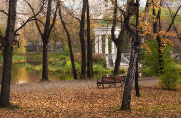 Autumn nature in a city park on a sunny day. An old white rotunda with columns and a round roof is...