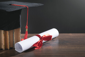 Graduation hat, book and diploma on the wooden table.