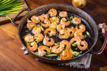 Fried shrimps in a pan, on a table with ingredients - green onions on a board