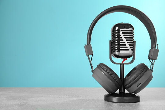 Microphone and modern headphones on grey table against light blue background, space for text