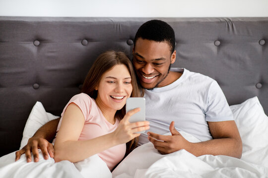 Happy Caucasian female and her black boyfriend looking at smartphone screen, chatting in social networks, searching web - Powered by Adobe