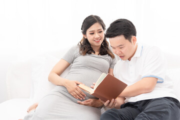 Obraz premium Asian new father spending time with his wife, excited dad expecting for newborn. Husband reading book to his wife preparing for new birth.