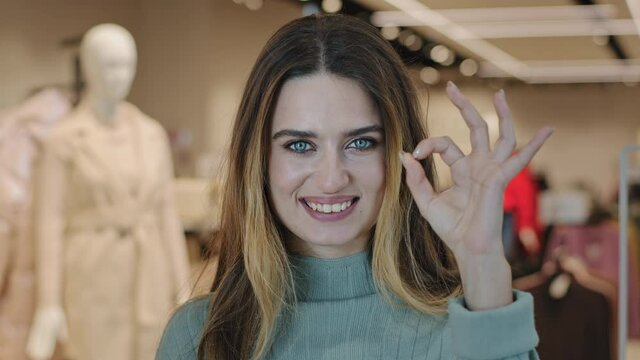 Portrait young caucasian woman client buyer young girl consumer close-up lady standing in clothing store in shopping center looking at camera shows okay everything fine good ok sign symbol agreeing