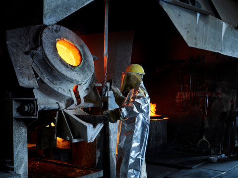 Blue-collar worker melting metal in furnace at industry