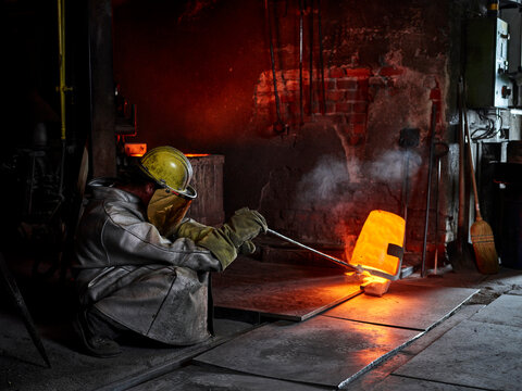 Craftsperson wearing protective workwear pouring cast metal in steel mill